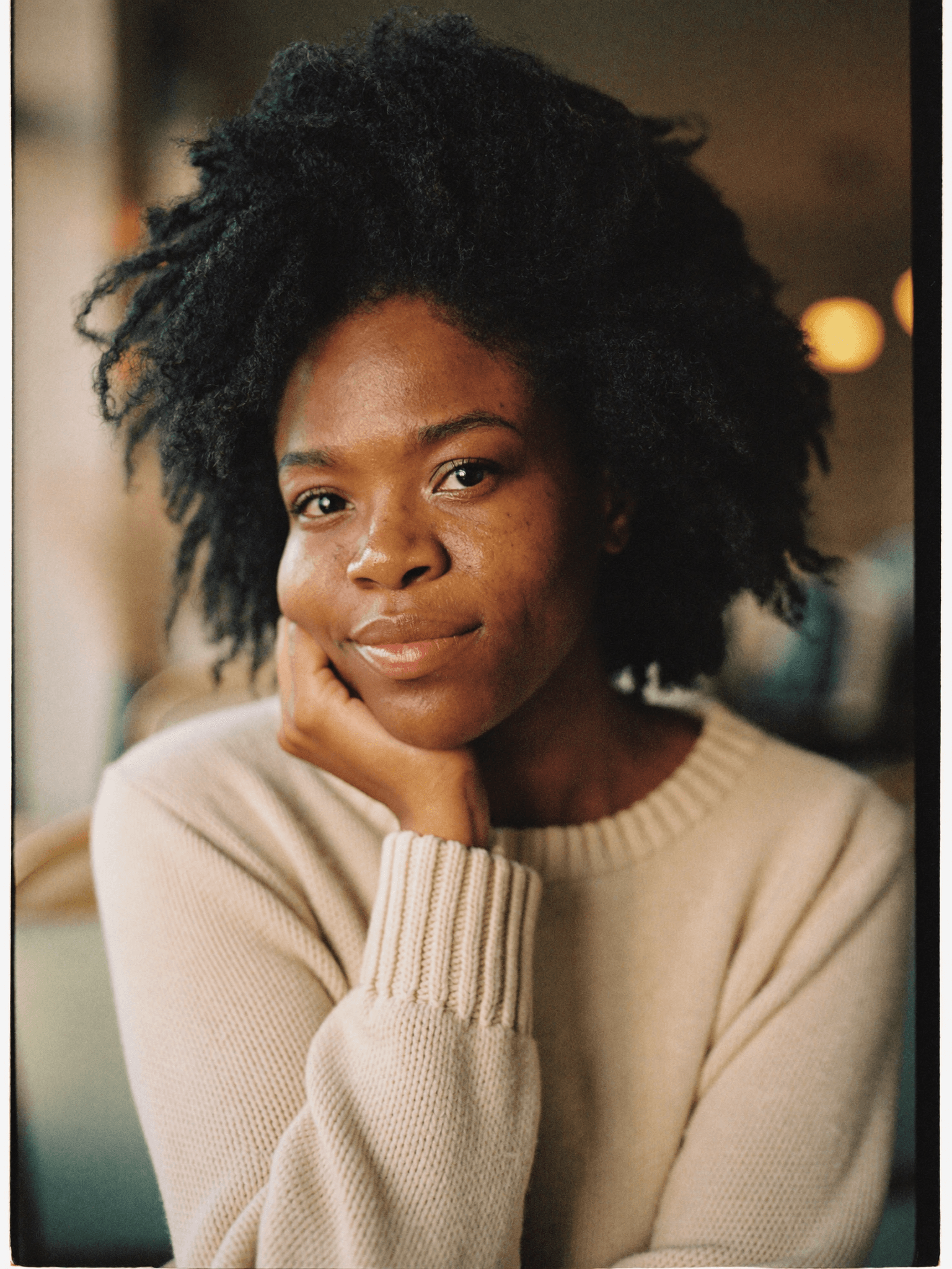 Woman in her early thirties with a warm direct gaze, cream knit sweater, warm cafe interior light